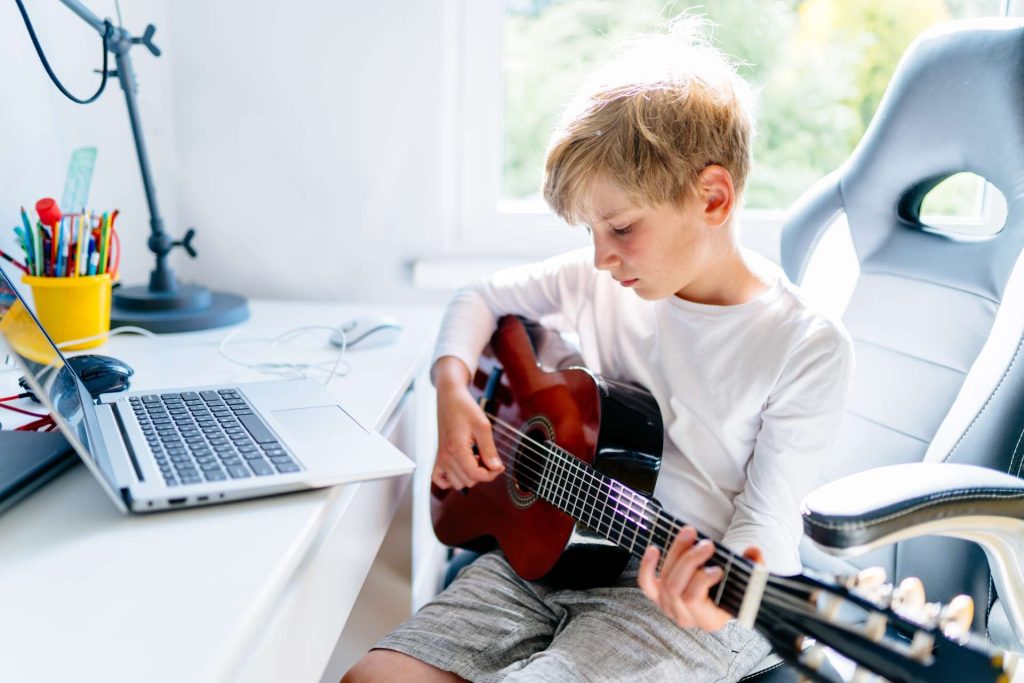 Lapsi opettelee soittamaan kitaraa verkkokurssin avulla.rkkokurssin äärellä.